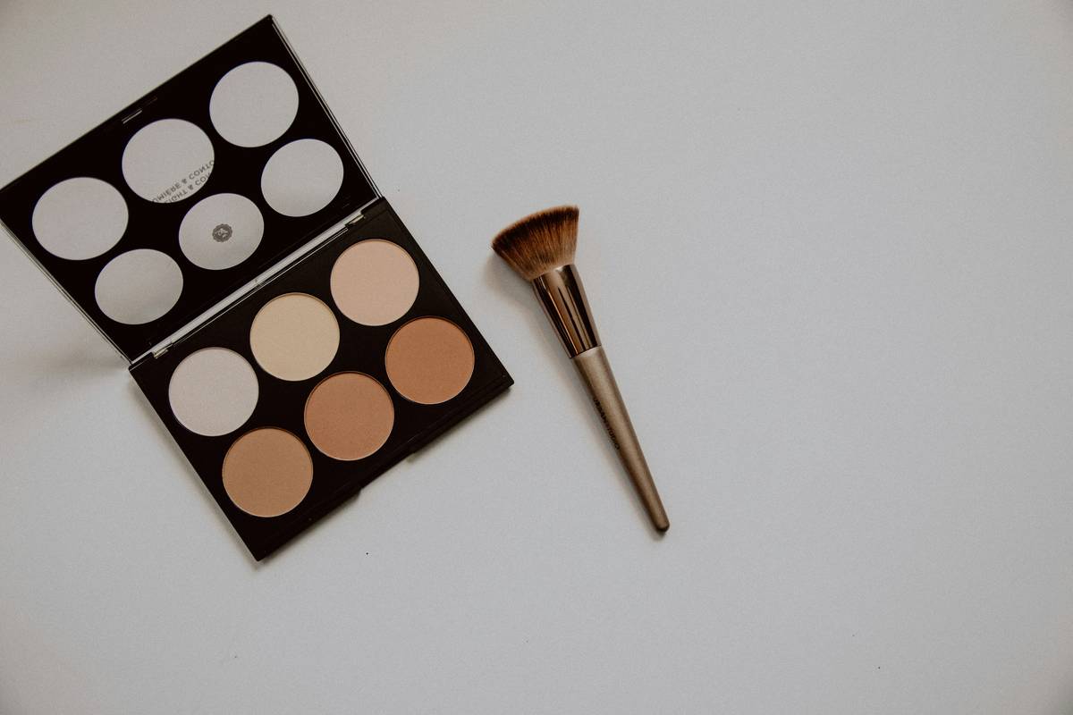 Close-up of hand holding a clean makeup powder sponge applying translucent setting powder to cheekbone